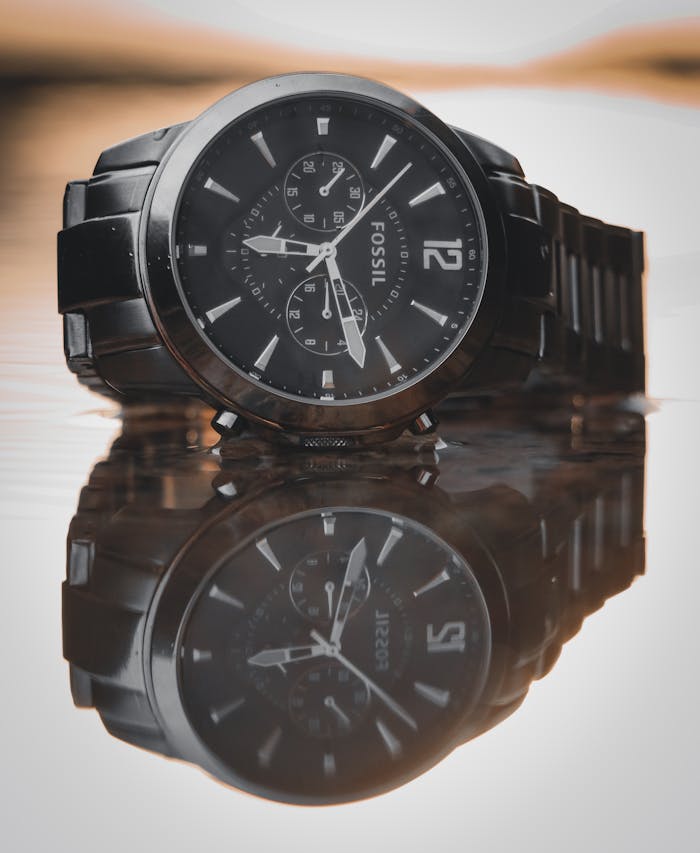 Close-up of a stylish black wristwatch reflecting on a smooth surface, showcasing its sleek design.